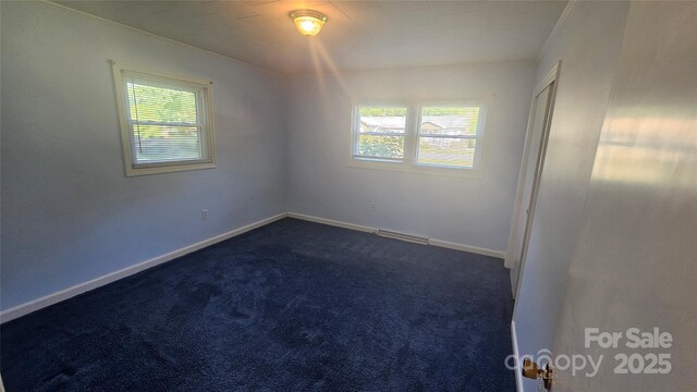 spare room featuring dark colored carpet and baseboards