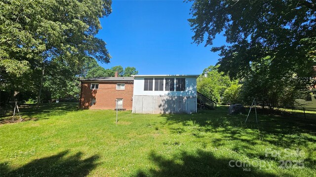 rear view of property featuring a yard, a chimney, brick siding, and stairway