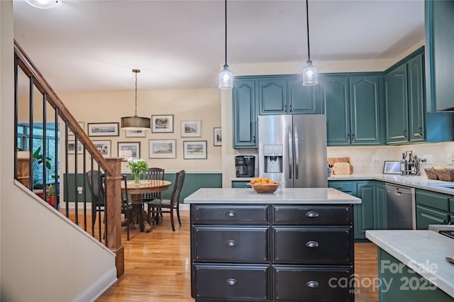 kitchen with appliances with stainless steel finishes, light countertops, decorative light fixtures, light wood-type flooring, and backsplash
