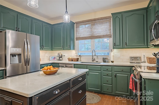 kitchen featuring stainless steel appliances, a sink, backsplash, light wood finished floors, and decorative light fixtures