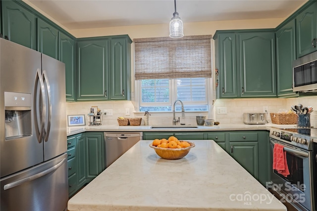 kitchen with appliances with stainless steel finishes, a sink, decorative backsplash, green cabinets, and hanging light fixtures