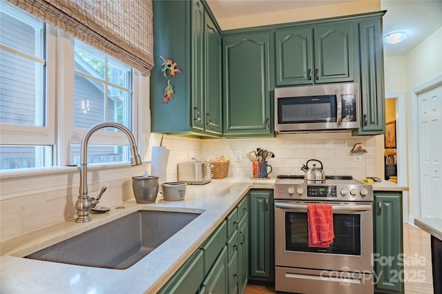 kitchen featuring appliances with stainless steel finishes, green cabinets, a sink, and tasteful backsplash