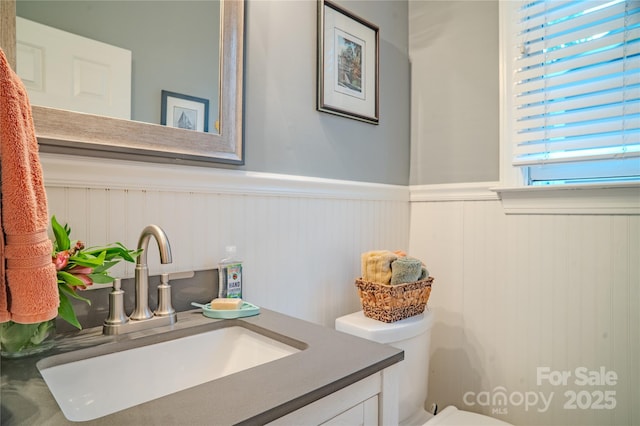 half bathroom with a wainscoted wall, vanity, and toilet