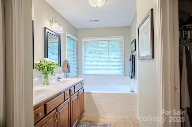 bathroom featuring healthy amount of natural light, a bath, double vanity, and tile patterned floors