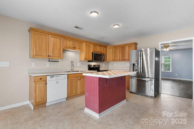 kitchen with appliances with stainless steel finishes, a sink, light countertops, a kitchen island, and baseboards