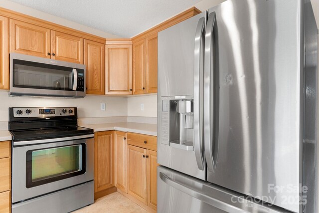 kitchen featuring stainless steel appliances, light countertops, light brown cabinetry, and light tile patterned flooring