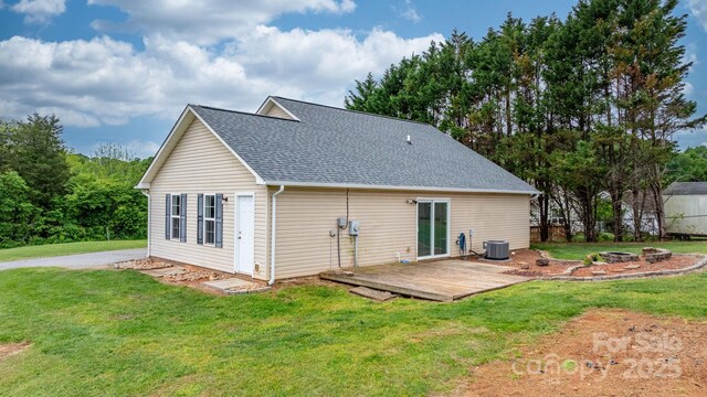 rear view of house featuring central AC, a deck, roof with shingles, and a lawn