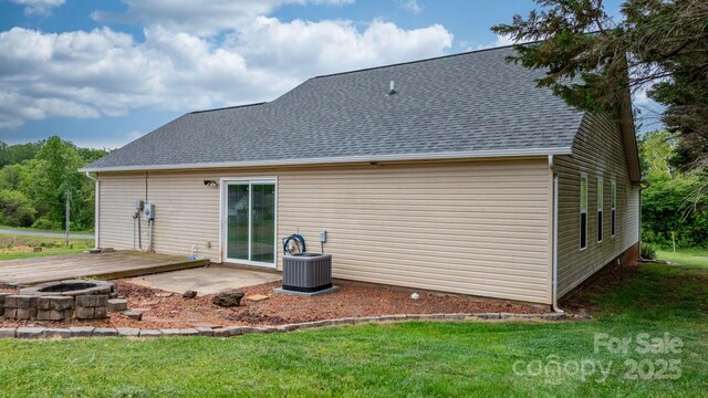back of house with cooling unit, a shingled roof, a fire pit, and a lawn