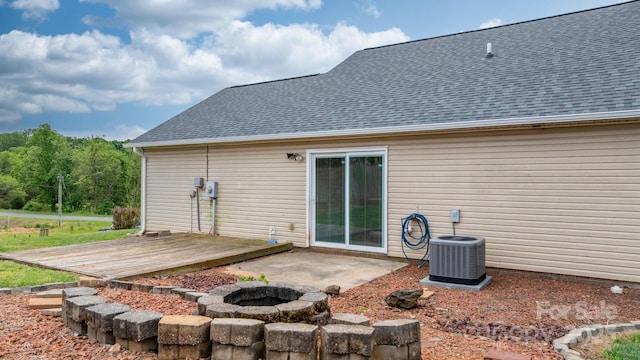rear view of house with a fire pit, central AC unit, a wooden deck, and roof with shingles
