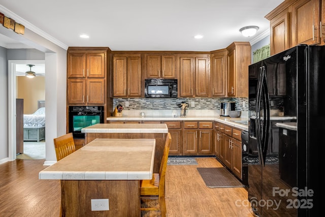 14 Phoenix Cir, Alexander, NC 28701 - kitchen with black appliances, a kitchen island, light wood-style flooring, crown molding, and decorative backsplash
