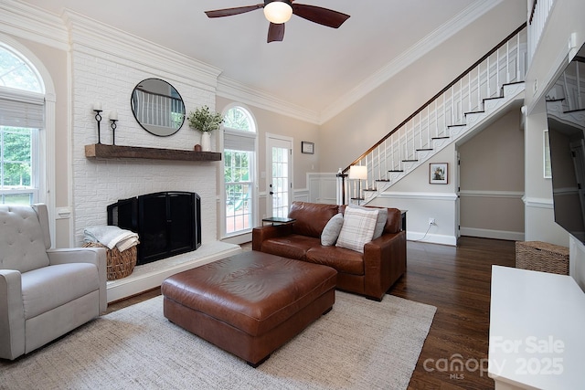 living area with stairs, a ceiling fan, healthy amount of natural light, wood finished floors, and crown molding
