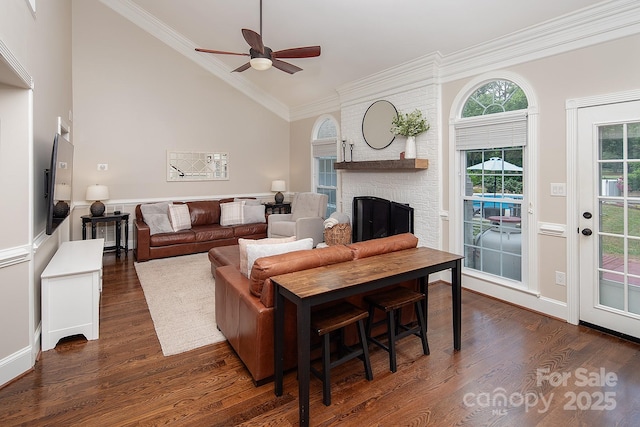 living area with a fireplace, dark wood-style flooring, vaulted ceiling, a ceiling fan, and crown molding
