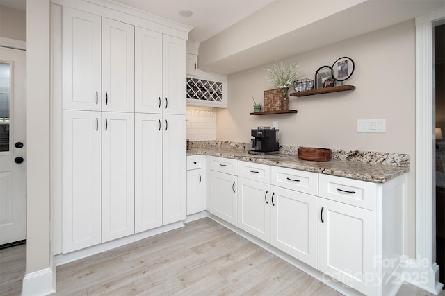 kitchen with open shelves, light wood-style floors, light stone countertops, and white cabinets