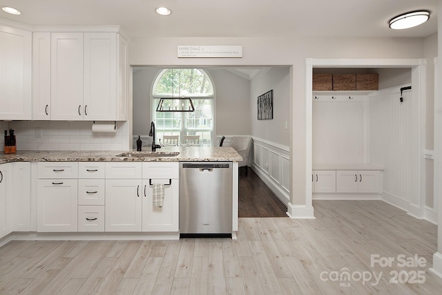 kitchen with stainless steel dishwasher, a sink, light wood finished floors, white cabinets, and light stone countertops