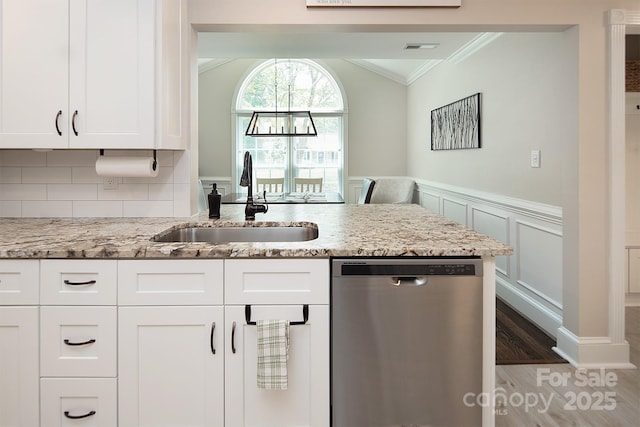 kitchen with stainless steel dishwasher, crown molding, a sink, light stone countertops, and white cabinetry