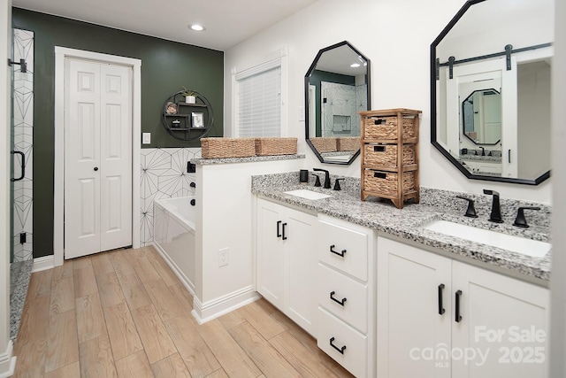 full bathroom with wood finished floors, a garden tub, recessed lighting, and double vanity