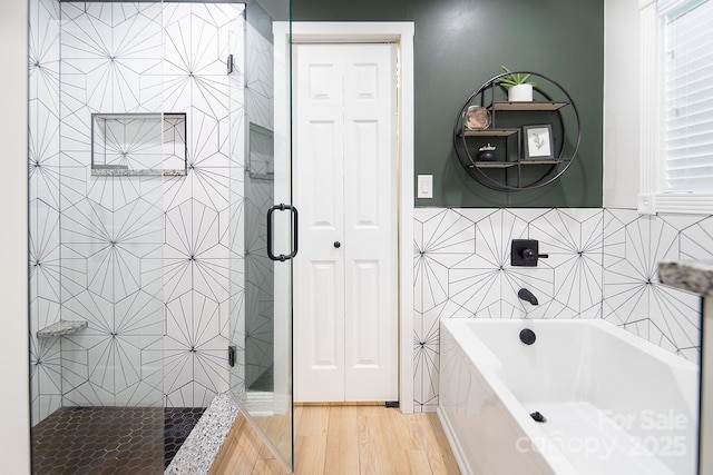 bathroom featuring a stall shower, a tub, wood finished floors, and tile walls