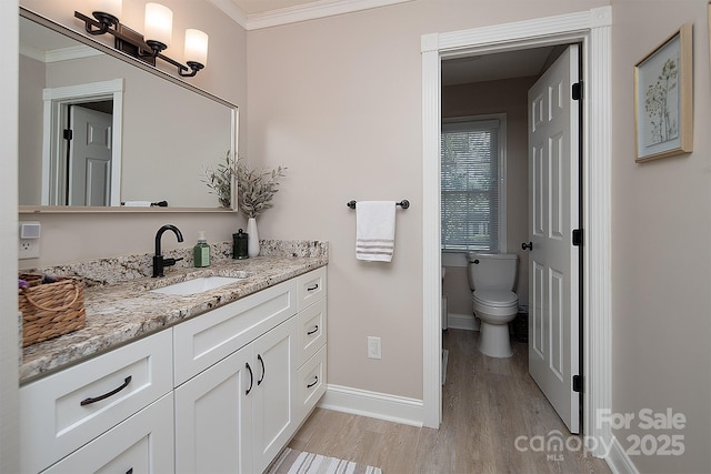 bathroom with wood finished floors, baseboards, crown molding, toilet, and vanity