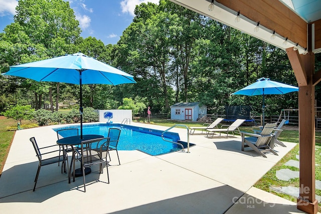 view of pool with fence, a patio area, view of scattered trees, an outbuilding, and a shed