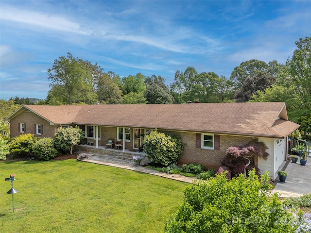 back of property featuring a garage, a lawn, brick siding, roof with shingles, and a patio area