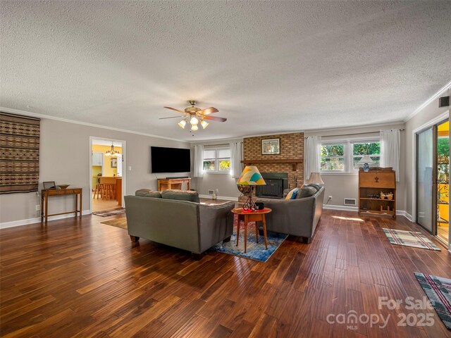 living room featuring dark wood-style flooring, a textured ceiling, a fireplace, a ceiling fan, and crown molding