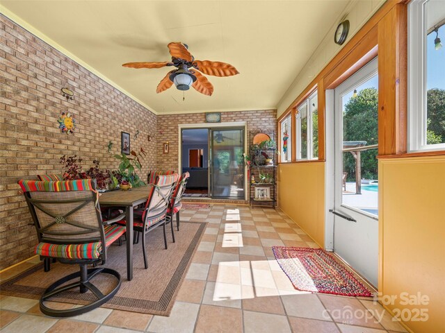 sunroom / solarium featuring brick wall, plenty of natural light, and baseboards