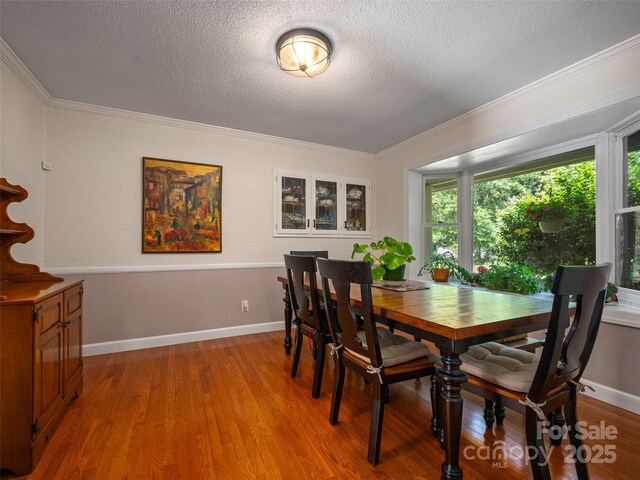 dining space featuring ornamental molding, light wood-style floors, a textured ceiling, and baseboards
