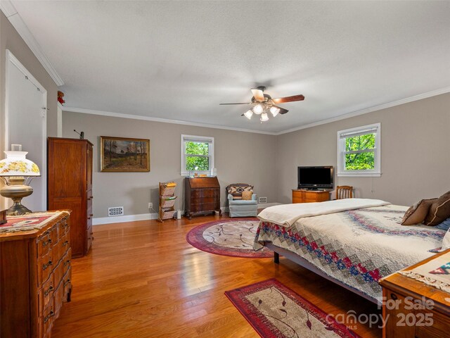 bedroom featuring light wood-style floors, crown molding, baseboards, and ceiling fan