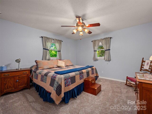 bedroom with light colored carpet, multiple windows, ceiling fan, baseboards, and a textured ceiling