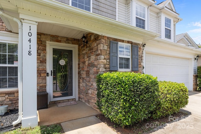 property entrance with stone siding, an attached garage, and concrete driveway