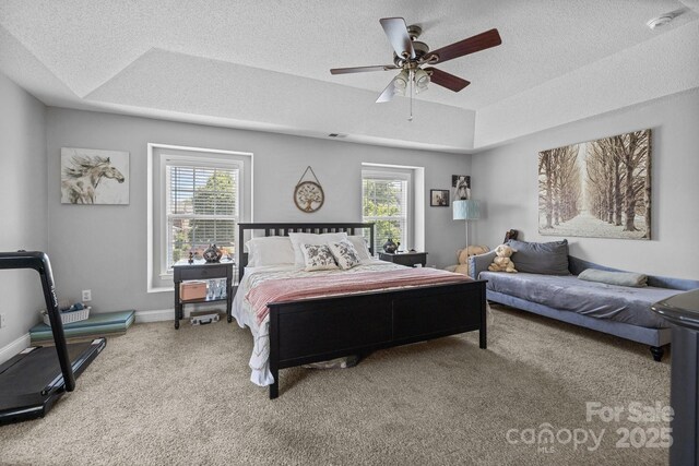 carpeted bedroom with multiple windows, a textured ceiling, ceiling fan, a tray ceiling, and baseboards