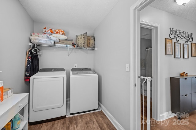 clothes washing area with washer and clothes dryer, wood finished floors, a textured ceiling, and baseboards