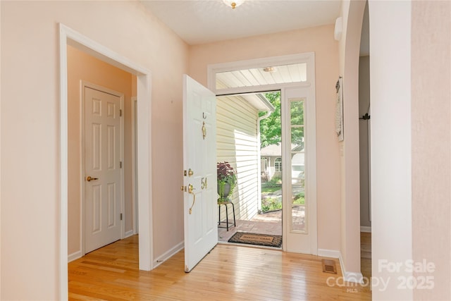 entryway with light wood-style flooring, arched walkways, and baseboards