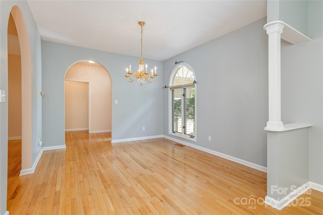 empty room with arched walkways, light wood-style floors, baseboards, and a chandelier