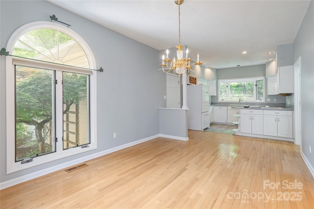 unfurnished dining area featuring light wood finished floors, a chandelier, baseboards, recessed lighting, and a sink
