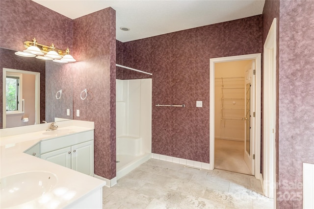 bathroom featuring a walk in shower, vanity, baseboards, and a spacious closet