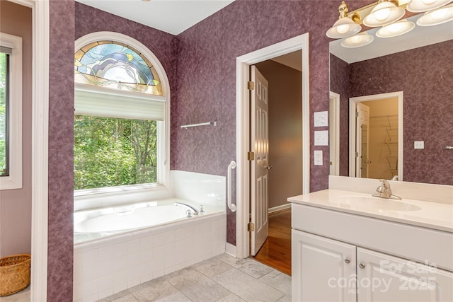 full bath with healthy amount of natural light, vanity, a bath, a walk in closet, and wallpapered walls