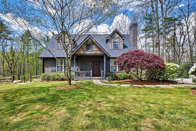 view of front of house featuring a chimney, covered porch, a front yard, and roof with shingles