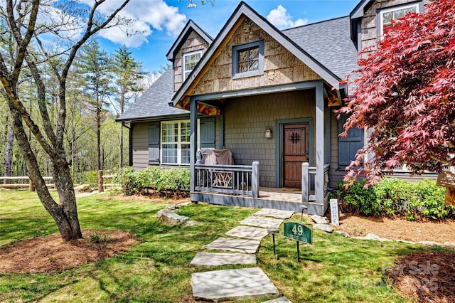 view of front of property featuring roof with shingles, covered porch, and a front yard