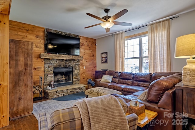 living area with wood finished floors, ceiling fan, a stone fireplace, and wooden walls