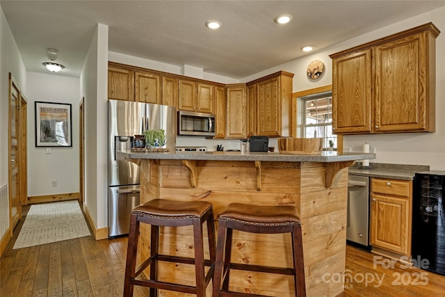 kitchen with appliances with stainless steel finishes, a kitchen breakfast bar, wine cooler, dark wood-style flooring, and recessed lighting