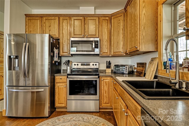kitchen with appliances with stainless steel finishes, a sink, dark wood-type flooring, and brown cabinetry