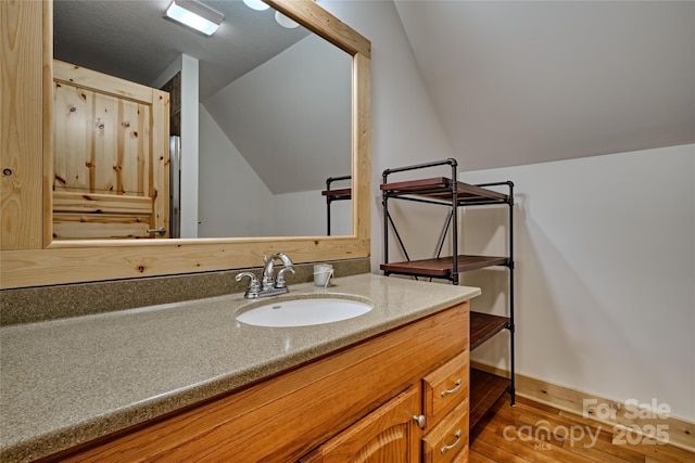 bathroom with wood finished floors, vanity, baseboards, and vaulted ceiling