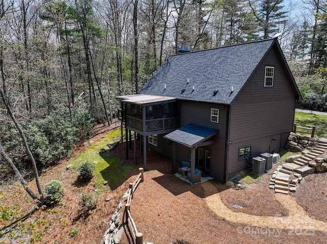 back of property featuring a sunroom, a shingled roof, stairway, central AC unit, and a patio