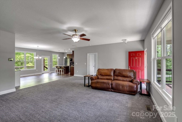 living area featuring dark carpet, a chandelier, baseboards, and a ceiling fan