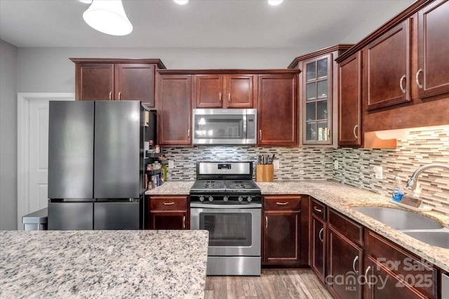 kitchen with appliances with stainless steel finishes, a sink, light wood-style floors, and light stone counters