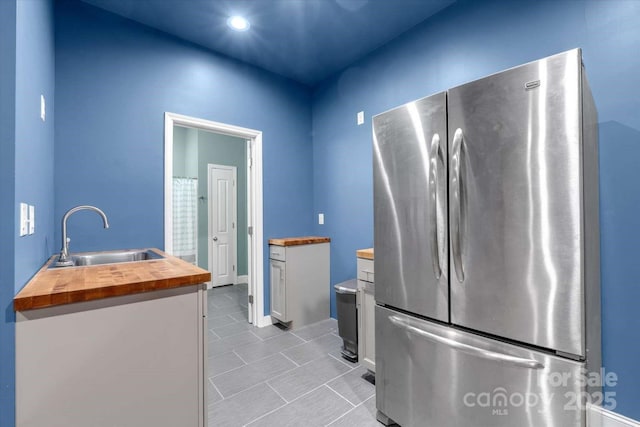 kitchen featuring freestanding refrigerator, wooden counters, a sink, light tile patterned floors, and white cabinets