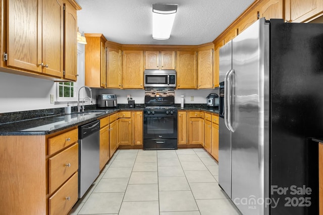kitchen featuring appliances with stainless steel finishes, a sink, a textured ceiling, light tile patterned floors, and brown cabinets