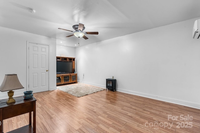 unfurnished living room featuring ceiling fan, light wood finished floors, baseboards, and a wood stove