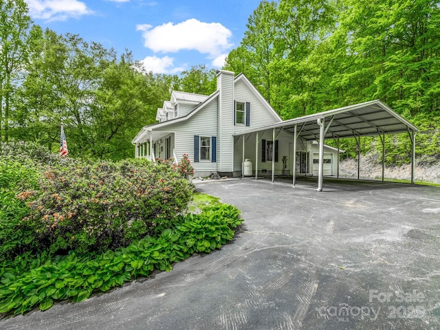 view of front facade with asphalt driveway, a carport, a chimney, and view of scattered trees
